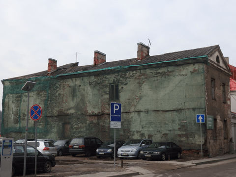 Deteriorated corner of historic building showing weathered surfaces with parking signs and parked cars